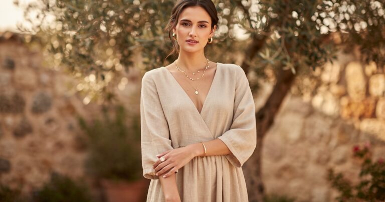 Femme en robe longue en lin beige portant des bijoux dores delicats dans un jardin mediterraneen